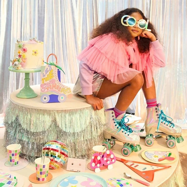 Kind auf Rollschuhen an bunt dekoriertem Partytisch mit Torte, Tellern, Bechern und schimmernder Partydeko.